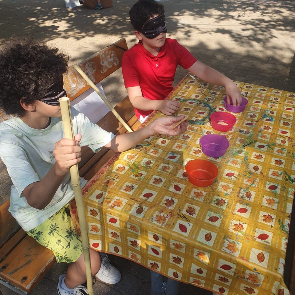 Zwei Kinder sitzen an einem Tisch, vor ihnen stehen für Schüsseln. Nur eine ist mit Snacks befüllt.