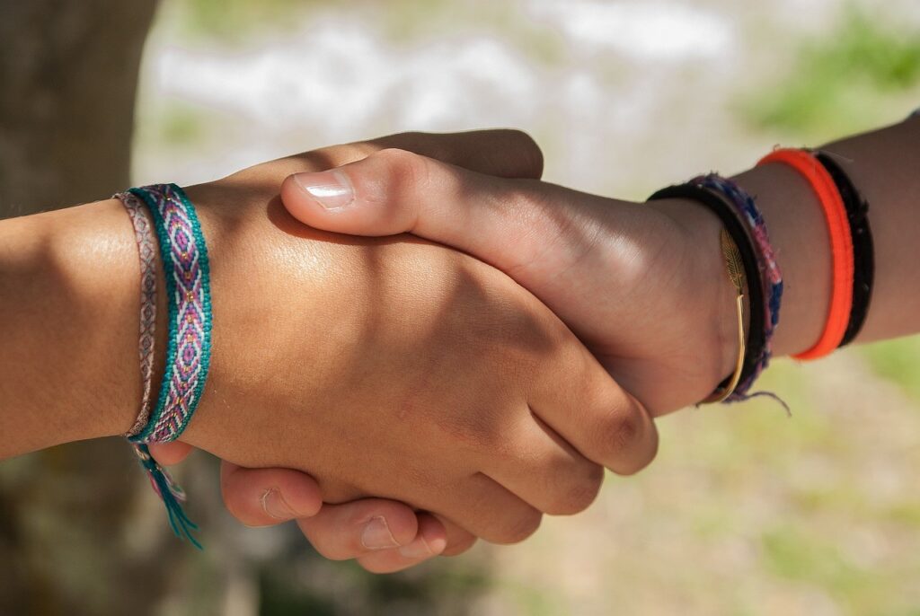 Zwei Hände, deren Handgelenke mit bunten Armbändern geschmückt sind, ineinander verschränkt.