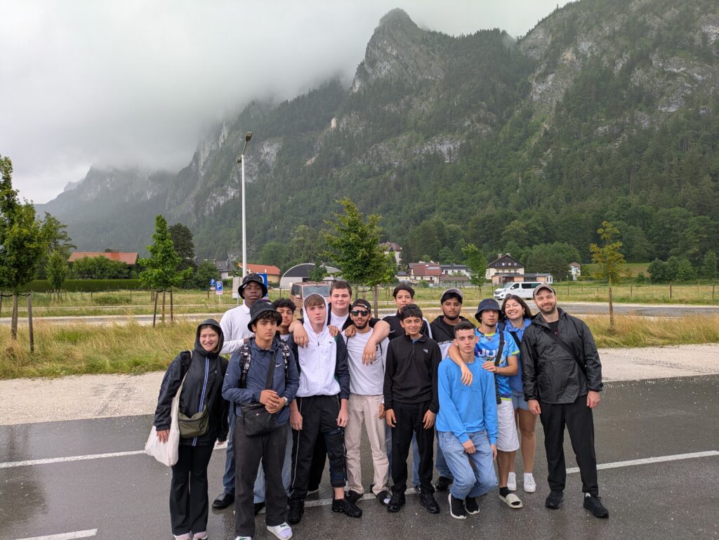 Ein Gruppenfoto von Jugendlichen und drei Erwachsenen, im Hintergrund befinden sich Berge.