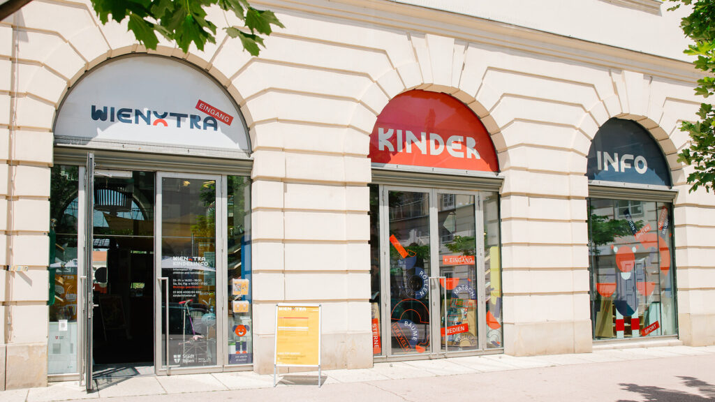Der Eingang der Kinderinfo, bestehend aus drei Glastüren, die in ein altes Gebäude eingebaut wurden.