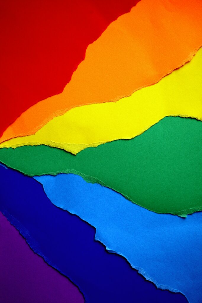 Übereinander gelegte Papierblätter in den Farben eines Regenbogens.