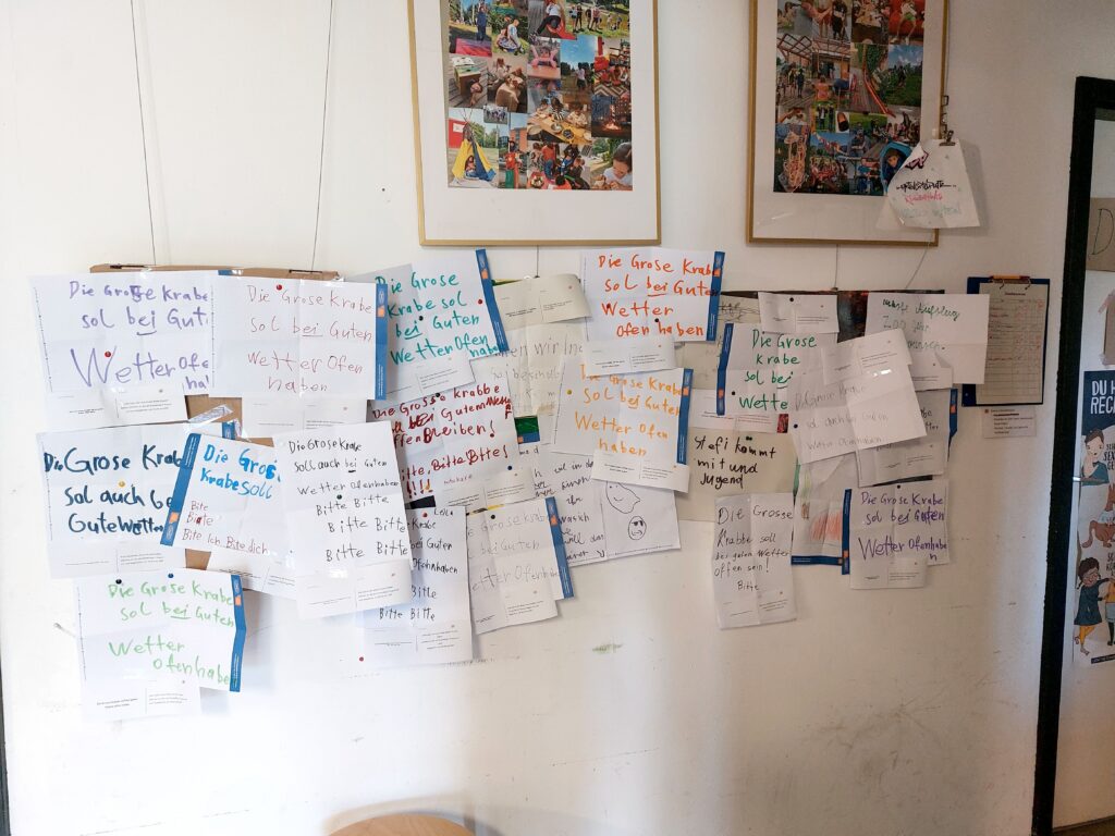 Viele, von Kindern geschriebene, Zettel hängen an einer Wand. Auf den meisten steht “Die große Krabbe soll bei schönem Wetter offen haben.”
