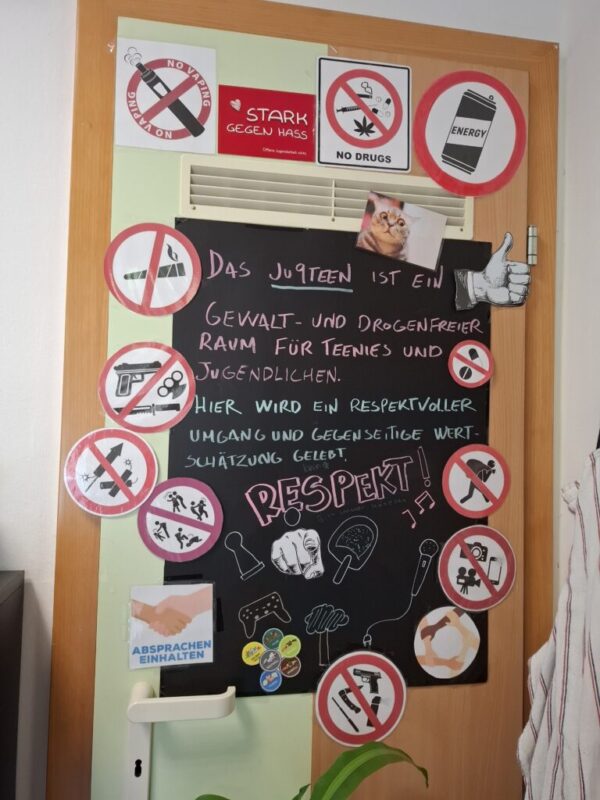 Auf einer Tür sind mit Kreidestift die Regeln auf eiener schwarzen Tafel aufgelistet wofür das JU9teen steht, die Tafel ist mit einigen Stickern umrahmt.