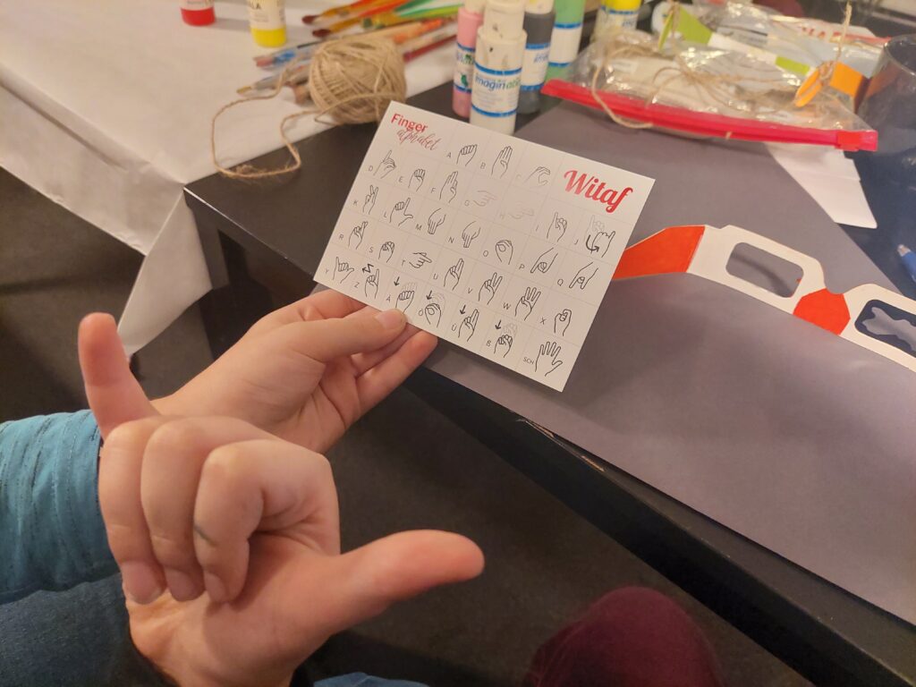 Die Hand eines Kindes stellt Gebärdensprache nach, die auf einen Zettel gedruckt ist.