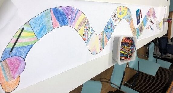 Ein langer Tisch auf dem sich eine bunte Zeichnung befindet, die einer Schlange ähnelt und ein Herz als Kopf hat.