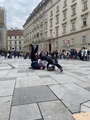 Drei tanzende Personen machen auf einem offenen Platz Hip Hop-Moves, im Hintergrund ist Publikum zu sehen.