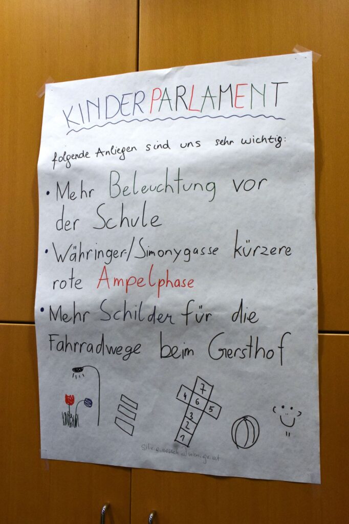 Ein Plakat mit der Überschrift „Kinderparlament“, auf dem drei Forderungen aufgelistet sind: Mehr Beleuchtung, längere Grünphasen und mehr Schilder für die Fahrradwege.