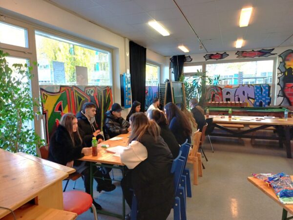 Schüler*innen sitzen an Holztischen in einem mit bunten Graffiti-Kunstwerken dekorierten Raum während einer SVS-Besprechung