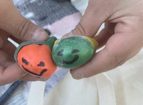 Ein orangener und ein grüner Stressball, auf die jeweils ein Gesicht gemalt wurde, werden von jeweils einer Hand gehalten.