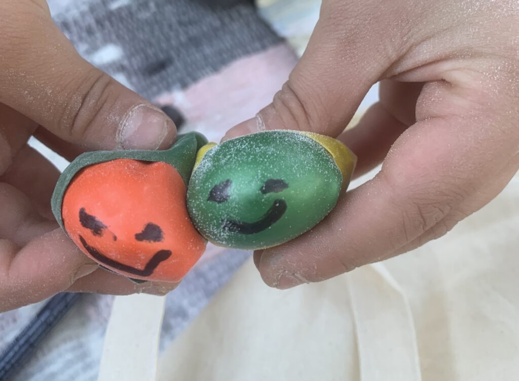 Ein orangener und ein grüner Stressball, auf die jeweils ein Gesicht gemalt wurde, werden von jeweils einer Hand gehalten.